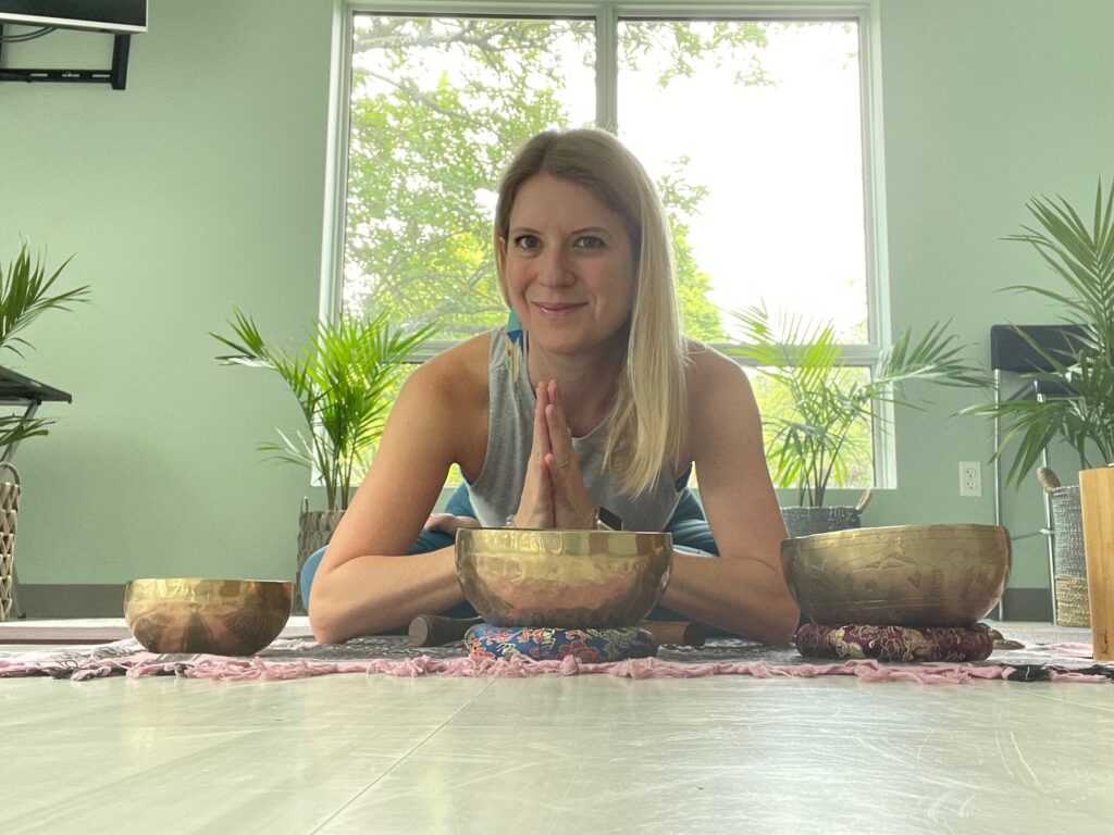 Jessica with hands in anjali mudra bowing toward singing bowls.